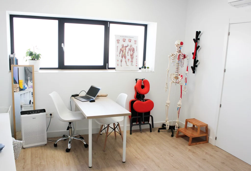 Sala de tratamientos de fisioterapia con mesa de terapeuta y silla de paciente